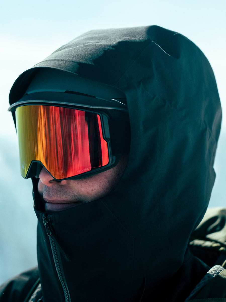 Skieur portant une lunette SPEK ajustée contre son casque, sous un capuchon, en montagne