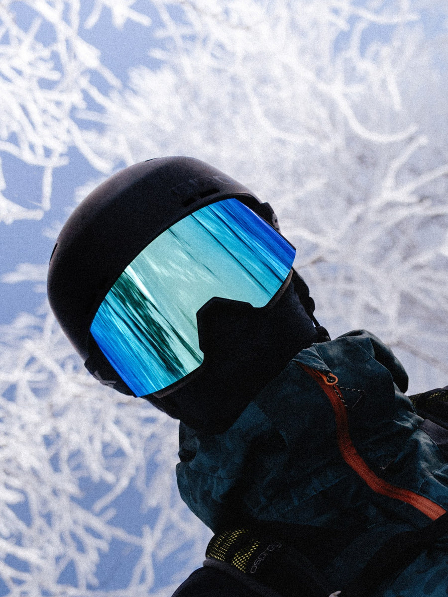 Skieur casqué portant la lunette SHIFT à lentille bleue devant des arbres givrés